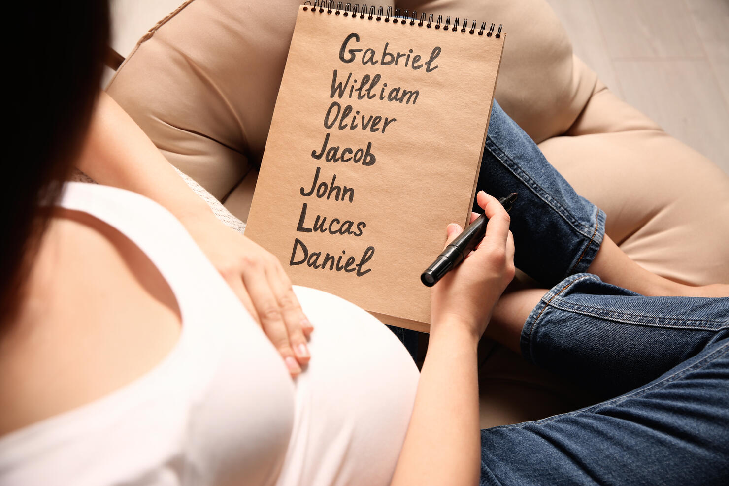 Pregnant woman with baby names list sitting in armchair, closeup