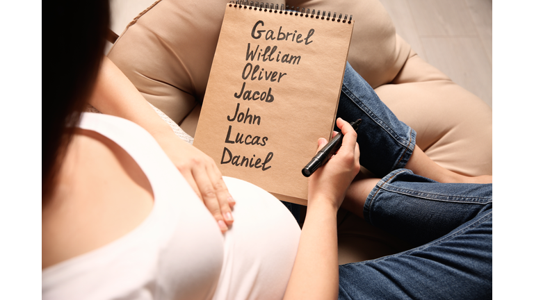 Pregnant woman with baby names list sitting in armchair, closeup