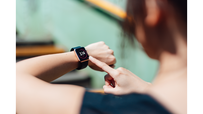 Over the shoulder view of young active woman using exercise tracking app on smart-watch to monitor her training progress after running