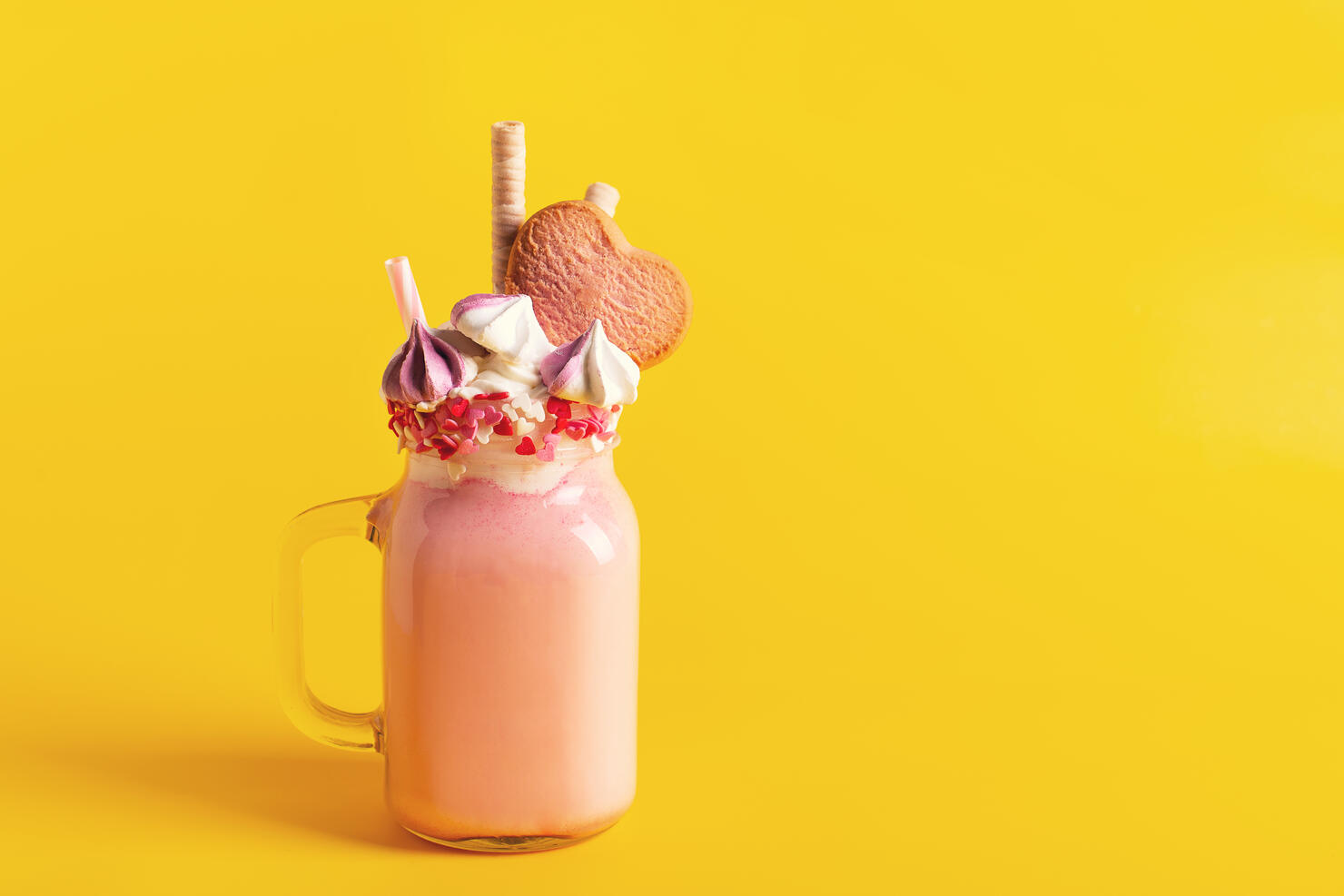 Pink milkshake with cream, marshmallow candy hearts on pink background