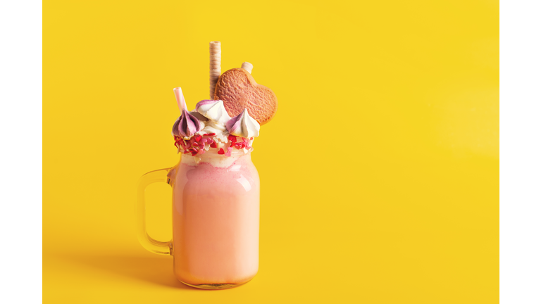 Pink milkshake with cream, marshmallow candy hearts on pink background
