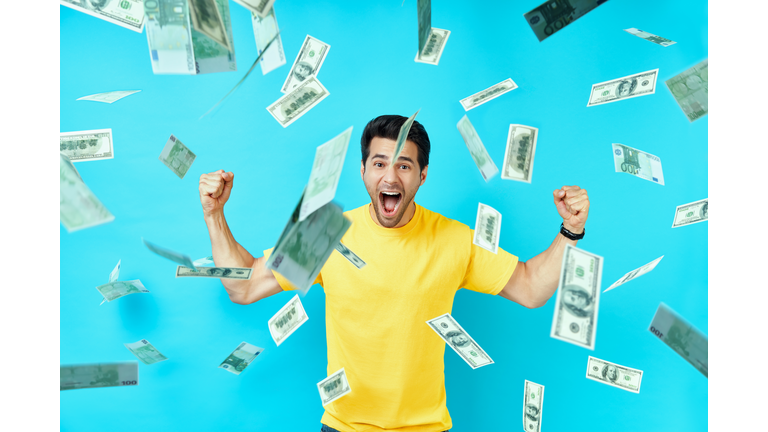 Happy excited man standing under money rain banknotes falling down