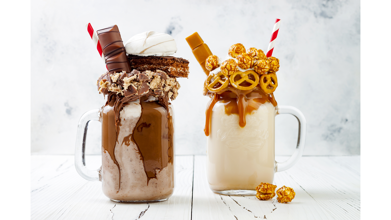 Caramel and chocolate indulgent exreme milkshakes with brezel waffles, popcorn, marshmallow, ice cream and whipped cream. Crazy freakshake food trend.