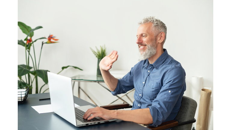 Cheerful mature grey-haired man using laptop for video call