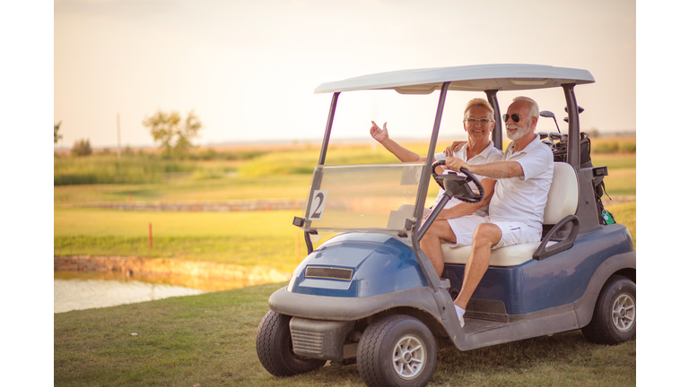 An elderly golf couple rides in a golf cart.