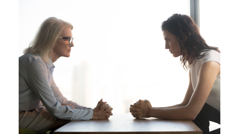 Young and old businesswomen sitting opposite, generations conflict at work