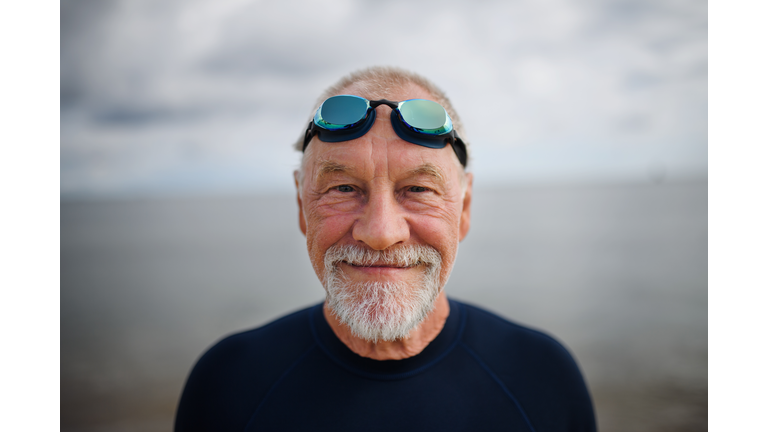 Portrait of happy actvie senior swimmer after early morning swim in sea, looking at camera.