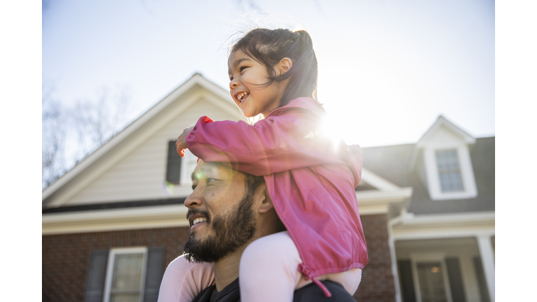 Daughter on father's shoulders in front of suburban home