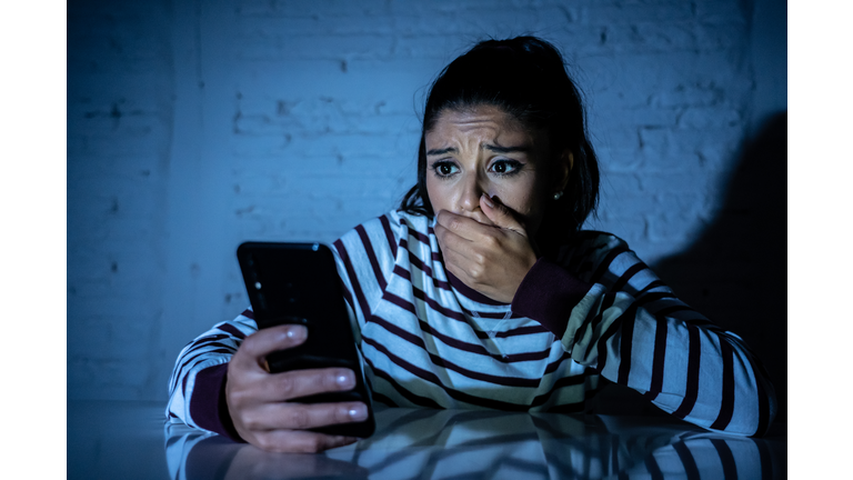 Frightened teenager or young woman using smart mobile cell phone as internet cyberbullying by message stalked abused victim.