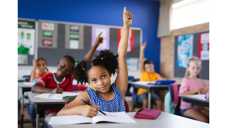 African american girl raising her hands while sitting on her desk in the class at school
