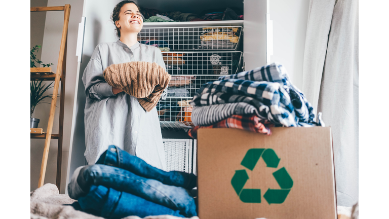 Recycle clothes concept. Young woman with recycling box full clothes.