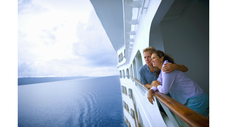Couple leaning on rail of cruise ship, looking at ocean