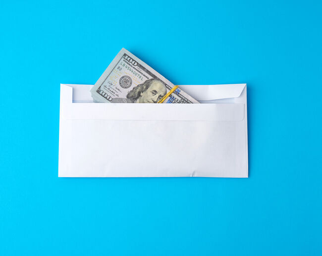 pack of paper American one hundred dollar bills tied with an elastic band and lies in a white envelope