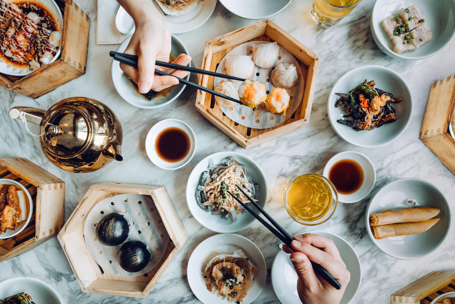 Flat lay of assorted traditional Chinese dim sum in bamboo steamer with a variety of appetitzers freshly served on table with two people enjoying meal and eating with chopsticks in restaurant. Chinese cuisine and food culture. Yumcha. Eating out lifestyle