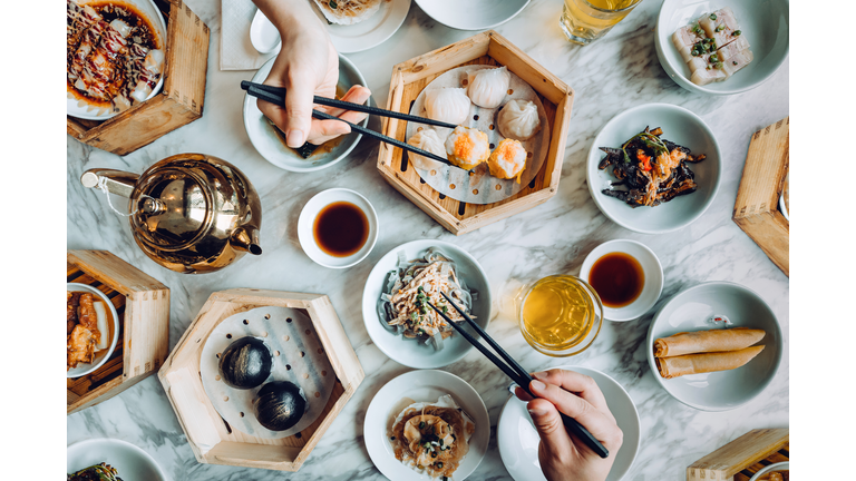 Flat lay of assorted traditional Chinese dim sum in bamboo steamer with a variety of appetitzers freshly served on table with two people enjoying meal and eating with chopsticks in restaurant. Chinese cuisine and food culture. Yumcha. Eating out lifestyle