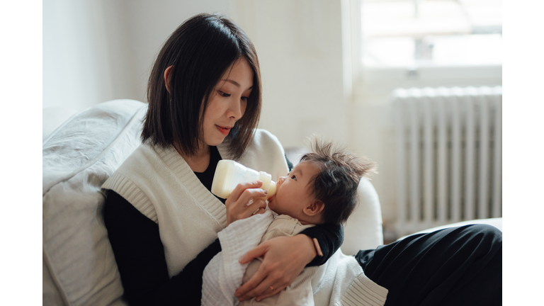 Mother feeding baby with bottle on sofa