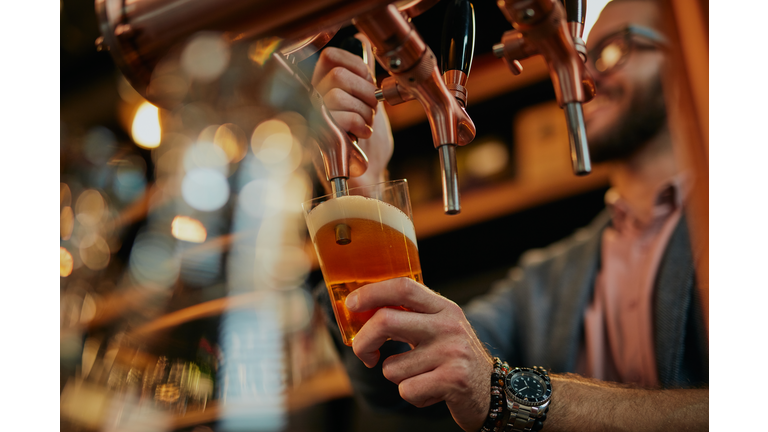 Tattooed caucasian barman pouring beer while standing in pub.