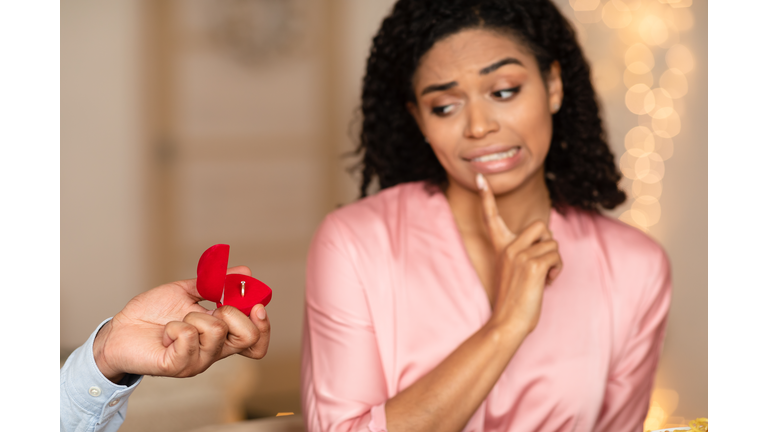 Black man making proposal with ring, confused woman rejecting