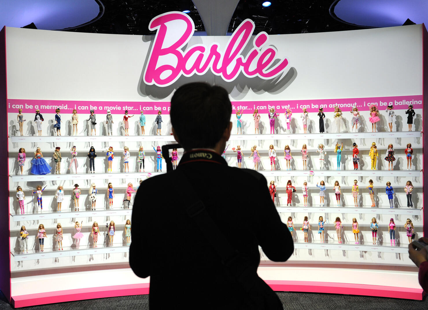 A woman photographs a wall of Barbie dol
