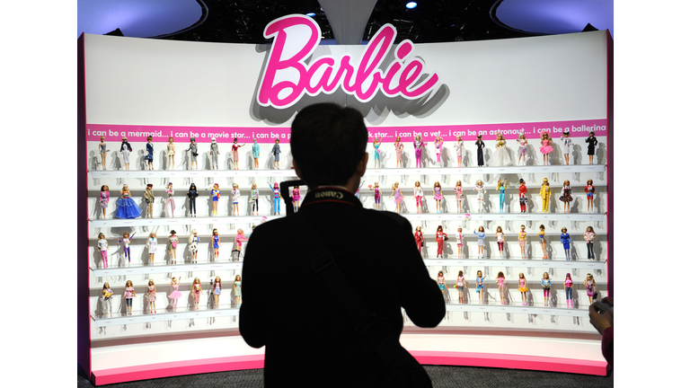 A woman photographs a wall of Barbie dol