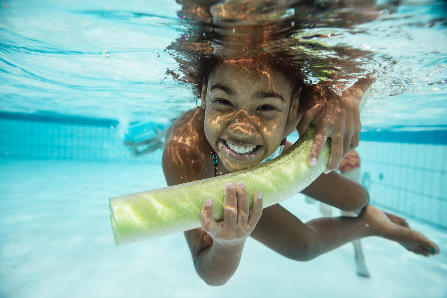 Portrait of smiling girl with pool noodle under water in swimming pool