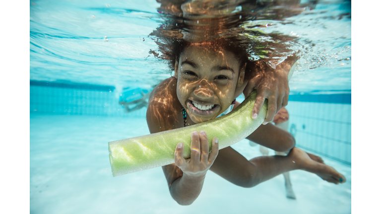 Portrait of smiling girl with pool noodle under water in swimming pool