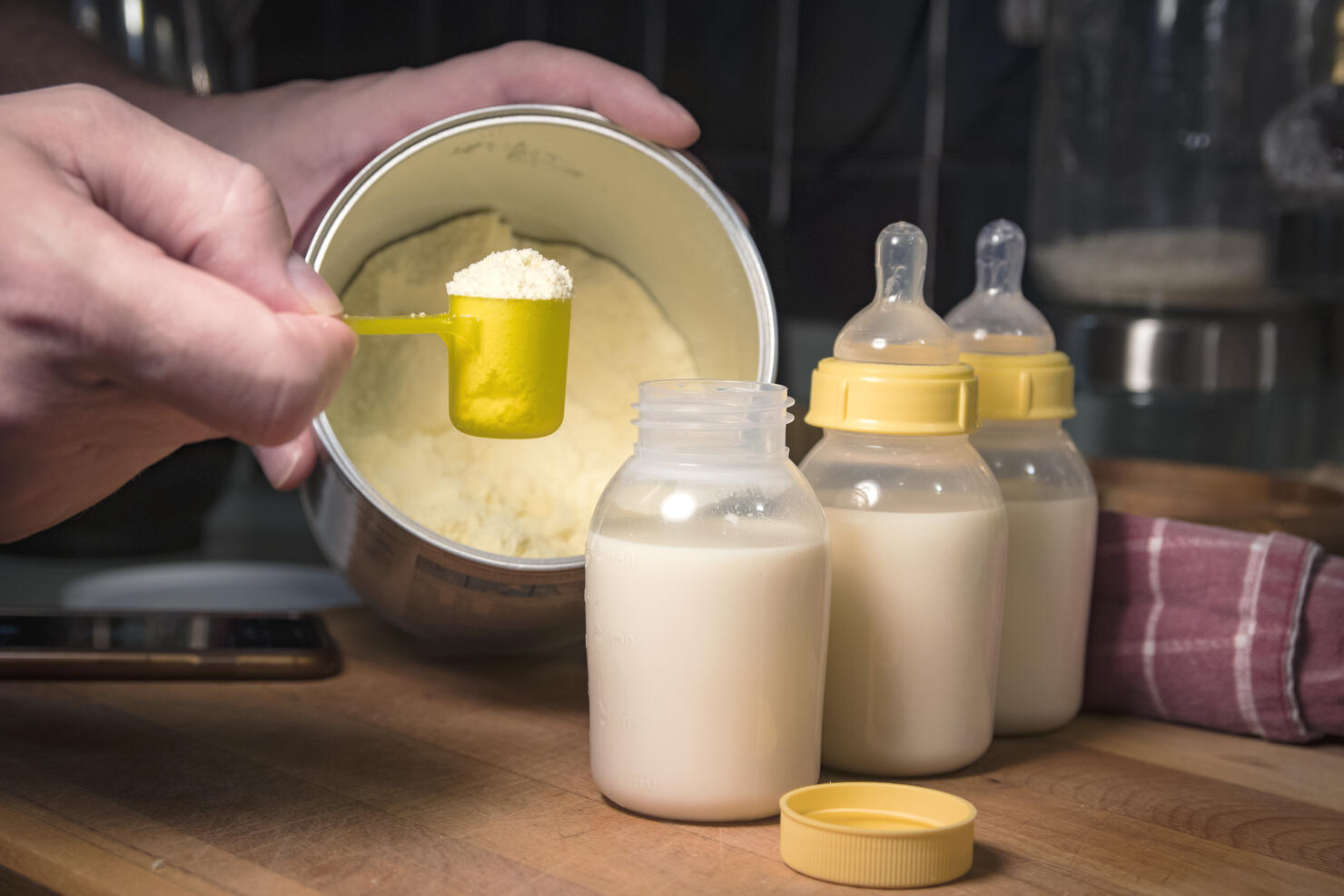 Hand holding scoop of powdered baby formula, ready to mix in bottles