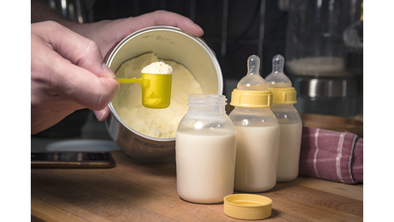 Hand holding scoop of powdered baby formula, ready to mix in bottles