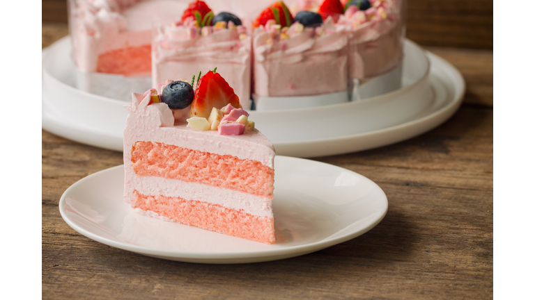 White chocolate strawberry yogurt cake decorated with fresh fruits and chocolate chunk on wood table. Delicious and sweet pink cake for Valentines or birthday party. Homemade bakery concept.
