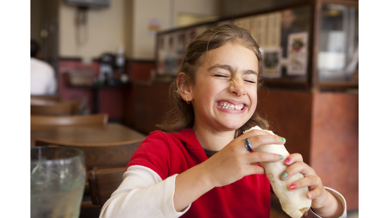 Mixed race girl eating burrito in restaurant
