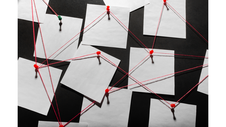 black detecftive board with blank paper linked by red thread.