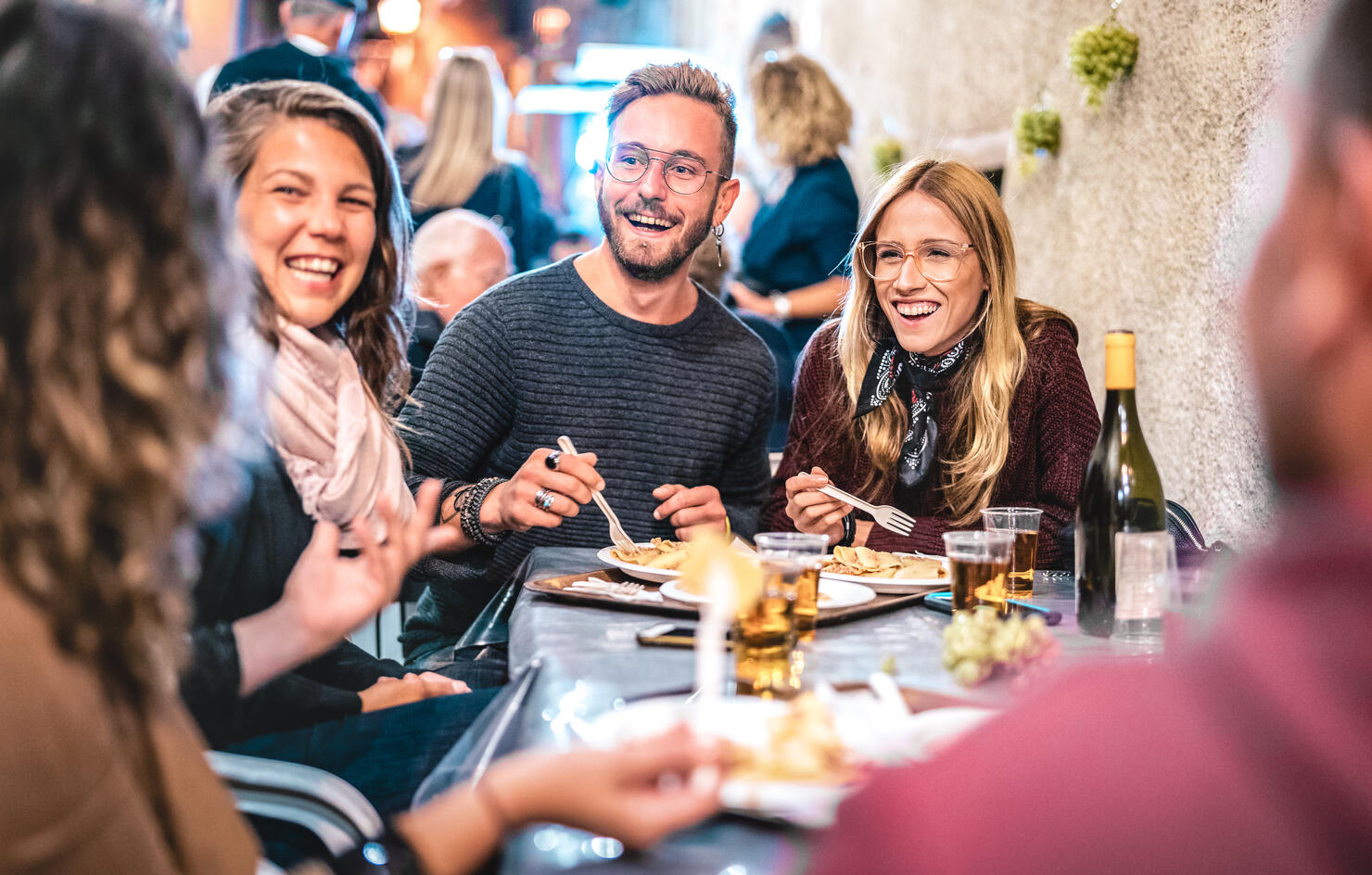 Young friends having fun drinking white wine at street food festival - Happy people eating local plates at open air restaurant together - Travel and dinning lifestyle concept on bulb light neon filter