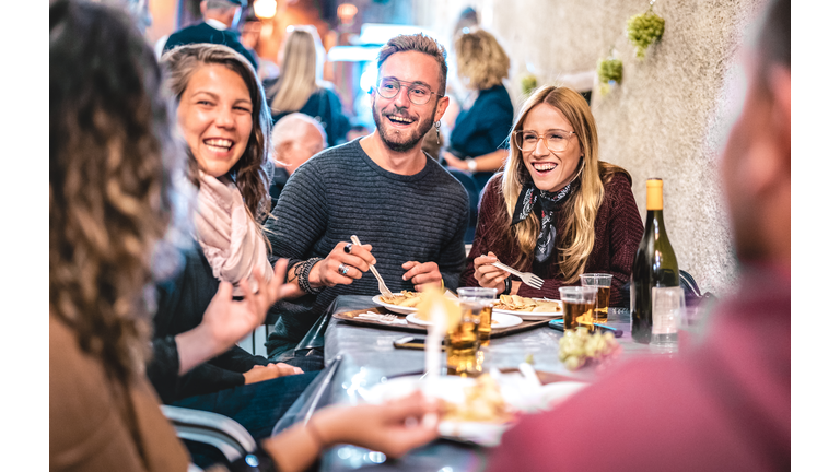 Young friends having fun drinking white wine at street food festival - Happy people eating local plates at open air restaurant together - Travel and dinning lifestyle concept on bulb light neon filter