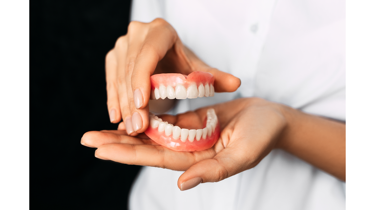 The dentist is holding dentures in his hands. Dental prosthesis in the hands of the doctor close-up. Front view of complete denture. Dentistry conceptual photo. Prosthetic dentistry. False teeth