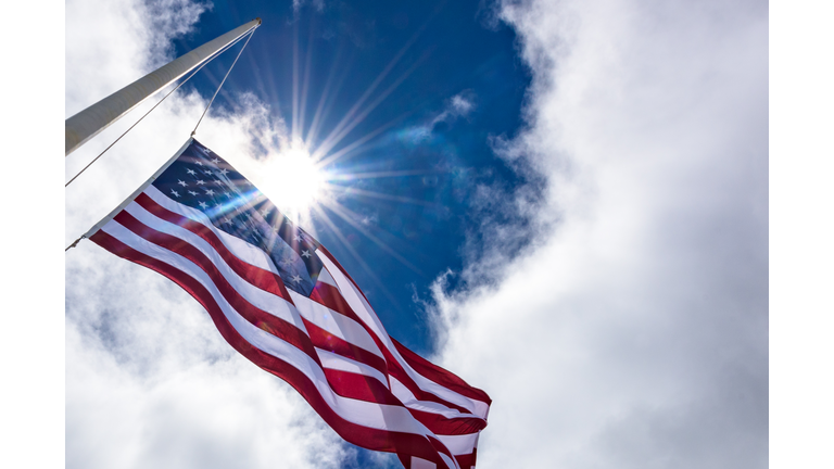 United States flag at half mast, looking up with sun