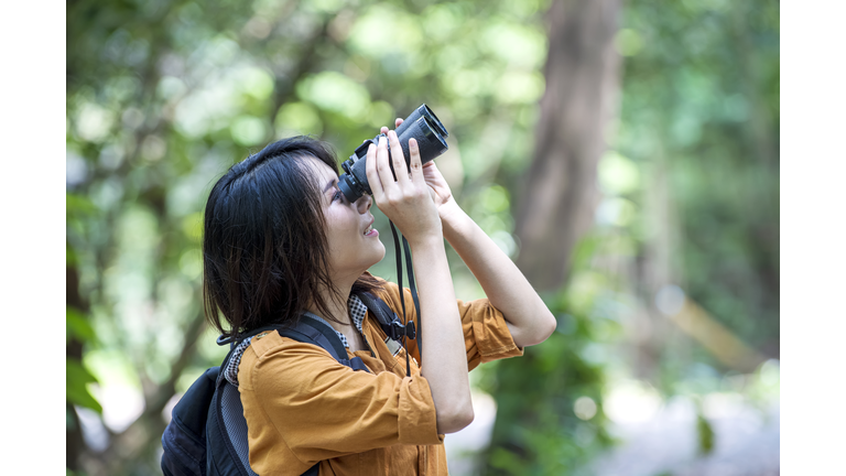 Cheerful young asian woman bird watching through binoculars. Nature lover concepts.