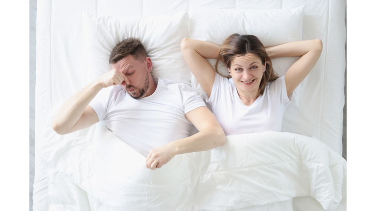 Married couple lying in bed. Man covering his nose with his hand