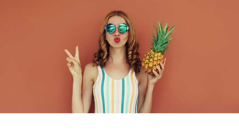 Summer portrait young woman blowing her lips with pineapple wearing a sunglasses posing on a brown background