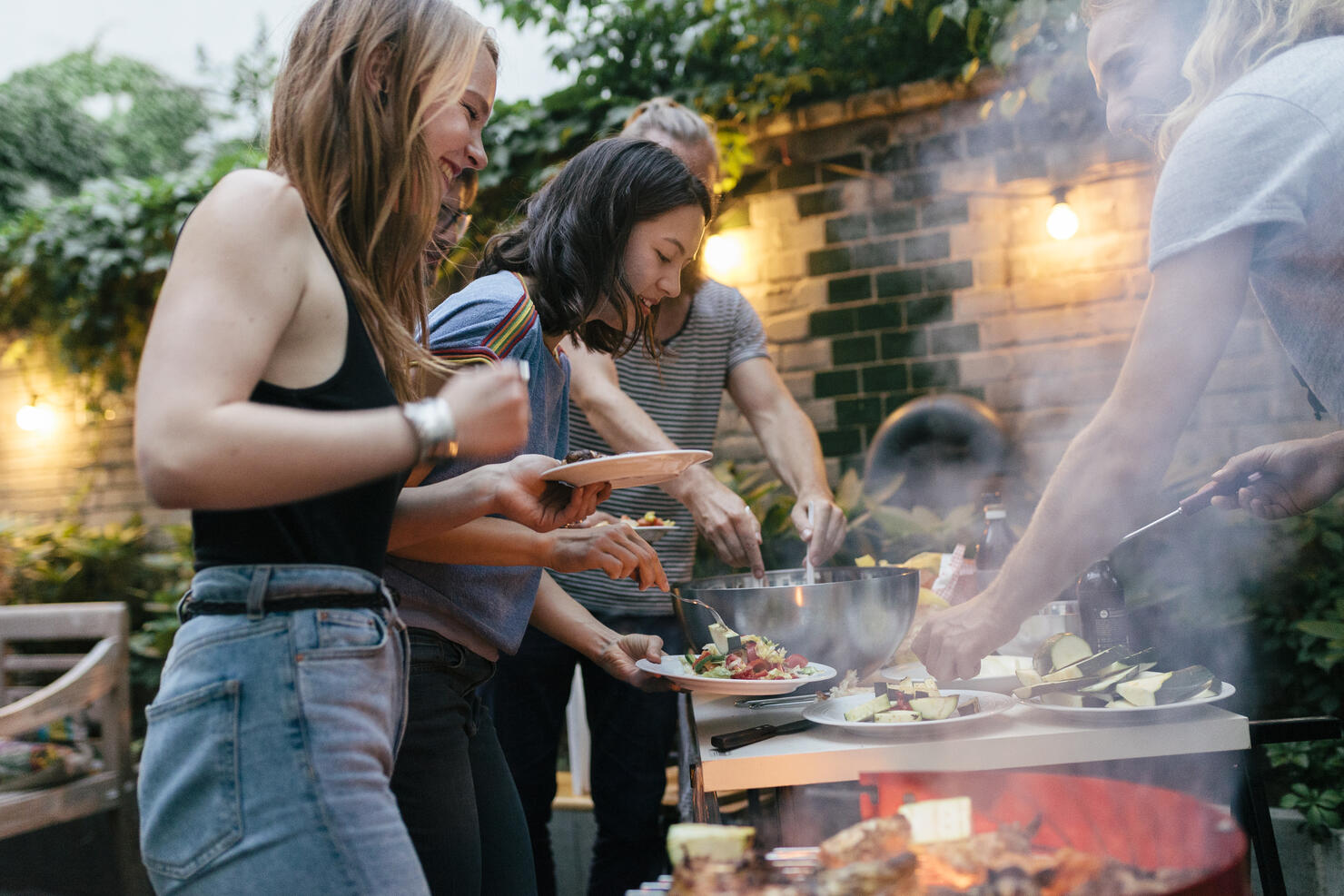 A Group Of Friends Helping Themselves To Food At A Summer Barbecue