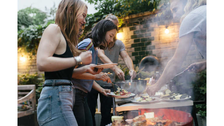A Group Of Friends Helping Themselves To Food At A Summer Barbecue