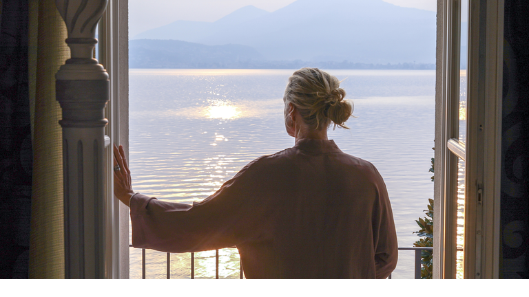 Mature woman walks out to veranda over a lake at sunrise