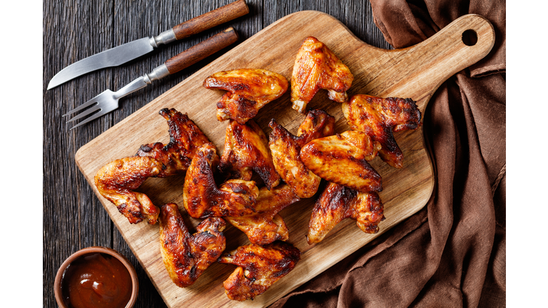 crispy fried chicken wings served on a wooden board with barbeque sauce on dark wooden table, flat lay