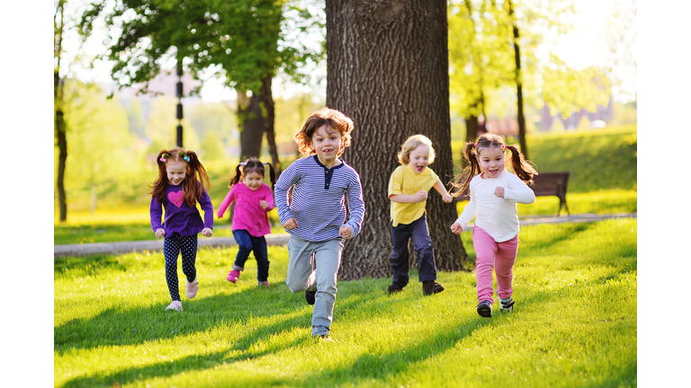 many young children smiling running along the grass in the park