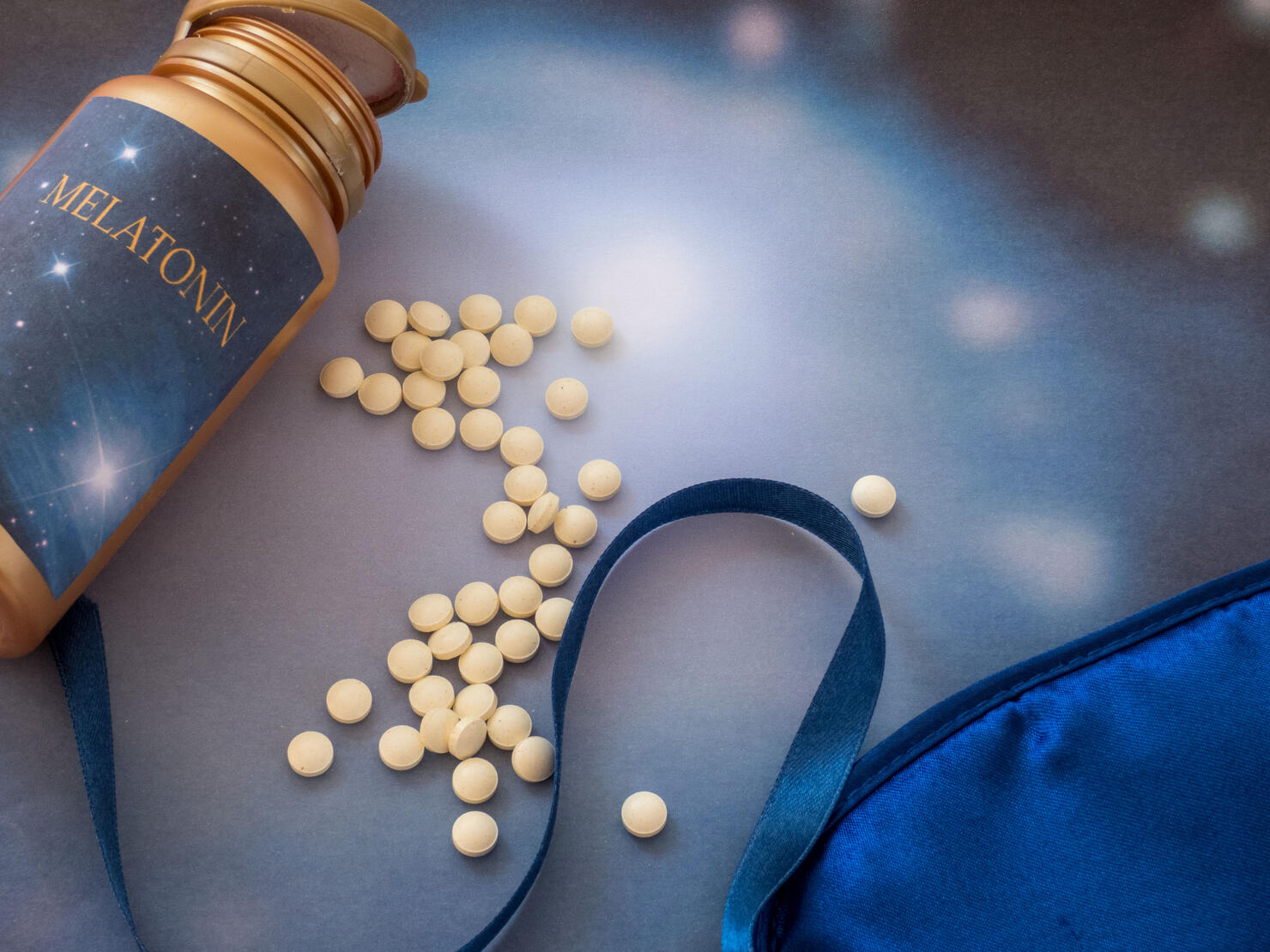 Melatonin supplements and sleep mask on the blue background
