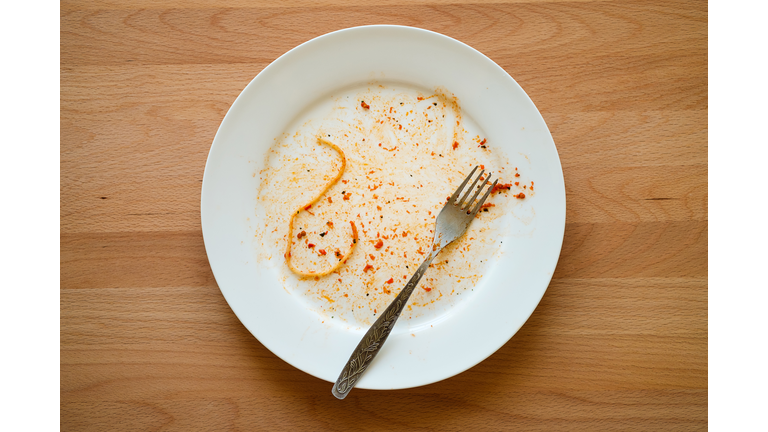 A dirty empty plate of pasta or spaghetti, a fork on a wooden table. Used cutlery, symbolize the end of lunch or dinner.