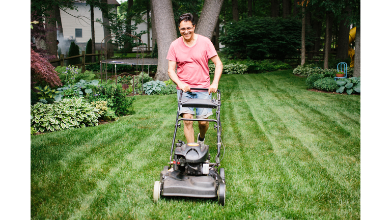 Smiling older man mowing the lawn in a backyard