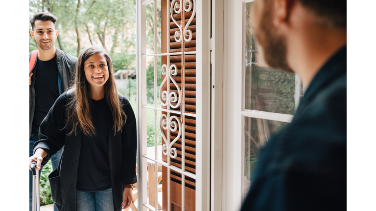 Midsection of male owner greeting guests at doorway of rental apartment