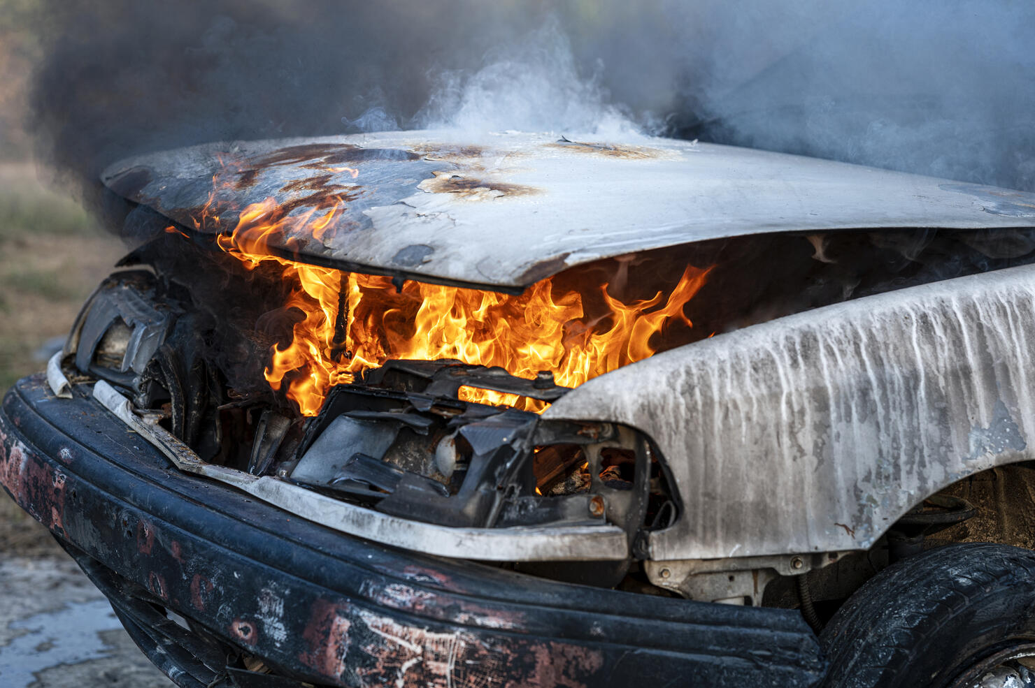 Close-up of burning car engine after a frontal crash collision on the roadside with flame and smoke.