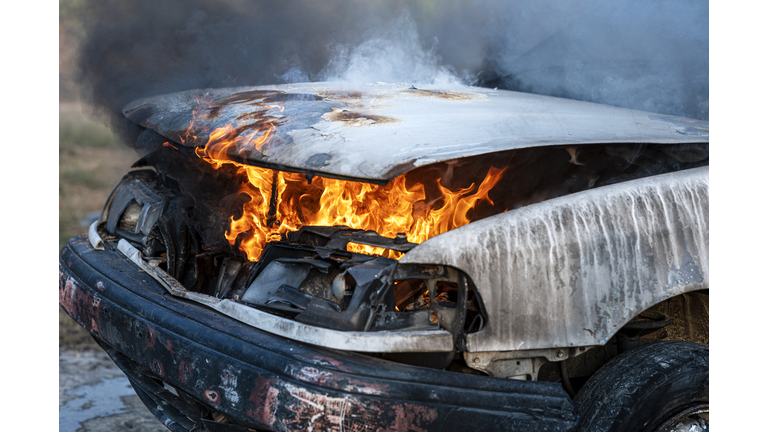 Close-up of burning car engine after a frontal crash collision on the roadside with flame and smoke.