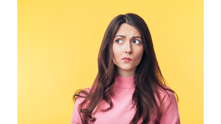 Thoughtful confused woman looking away isolated over yellow background